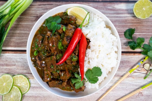 Bowl of hot and sour beef curry with garnish and rice