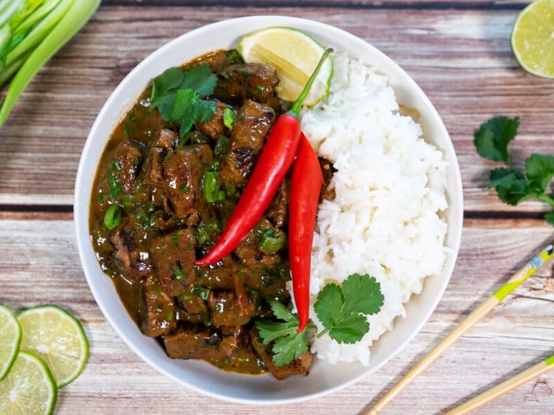 Bowl of hot and sour beef curry with garnish and rice