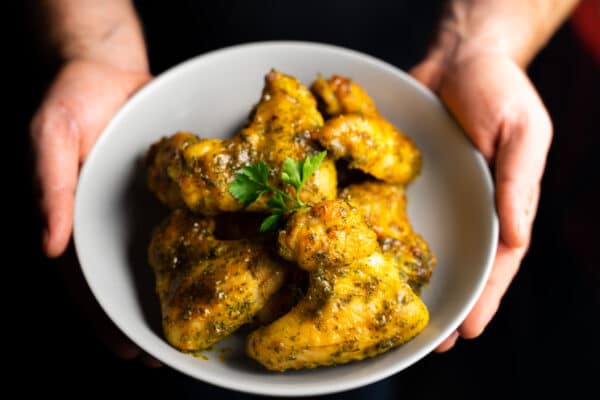 Chef holding bowl of garlic butter glazed chicken wings