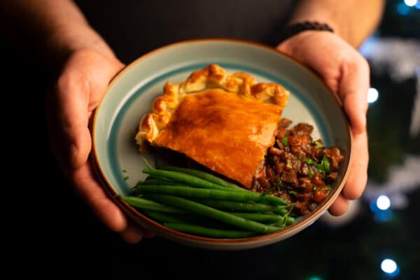 Chef holding plate of Beef and Mushroom pie served with green beans